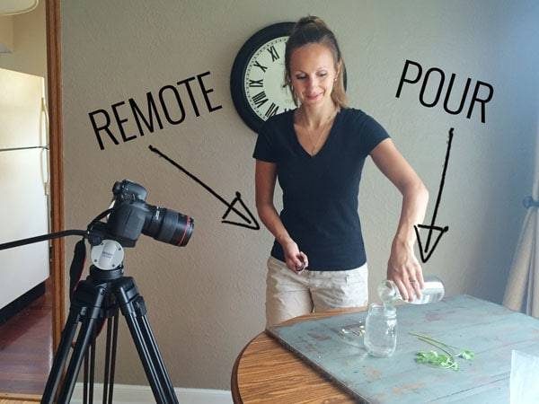 Tripod with camera and woman pouring water into a jar.