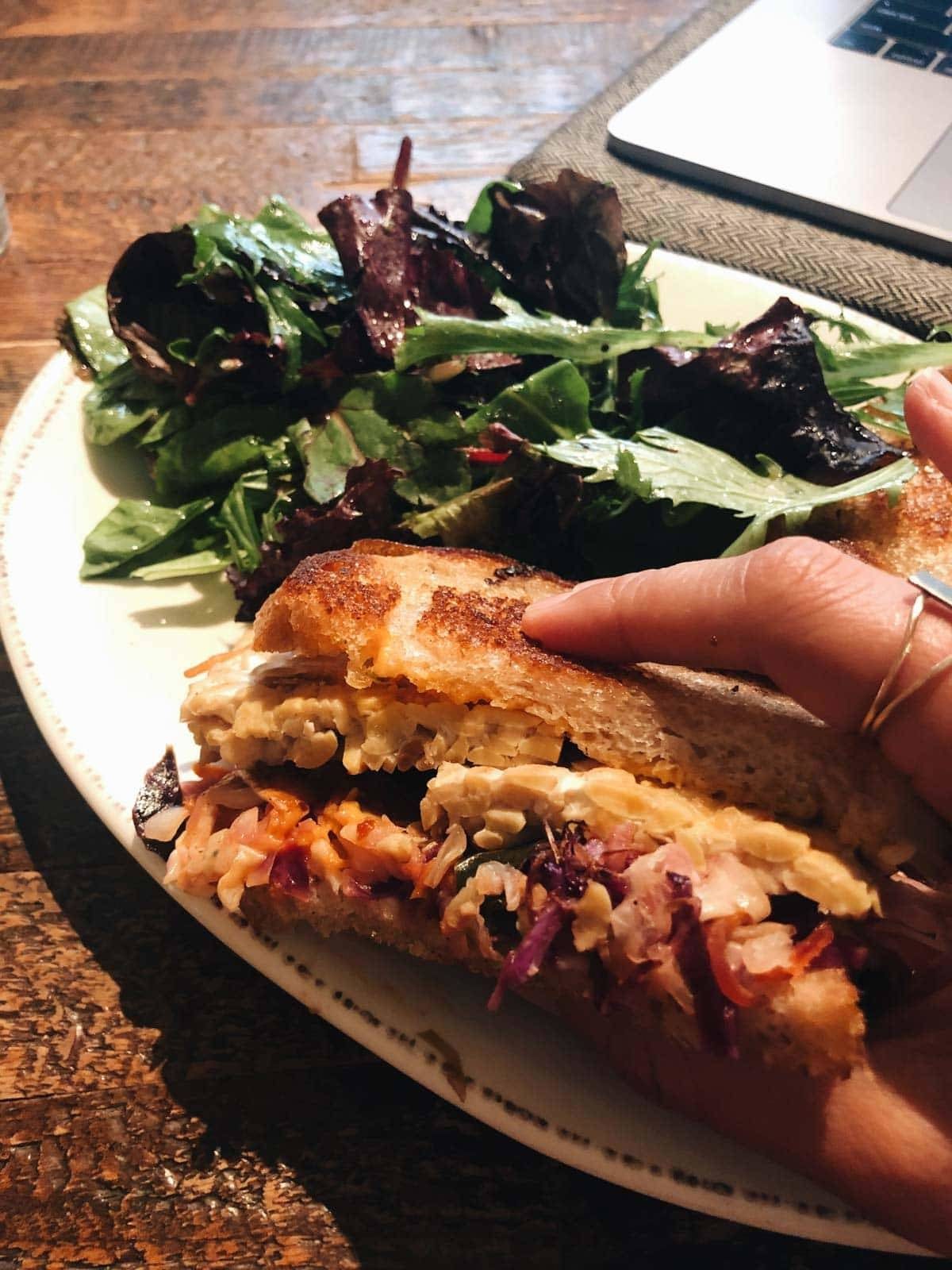 A person holding a sandwich on a plate with a small salad.