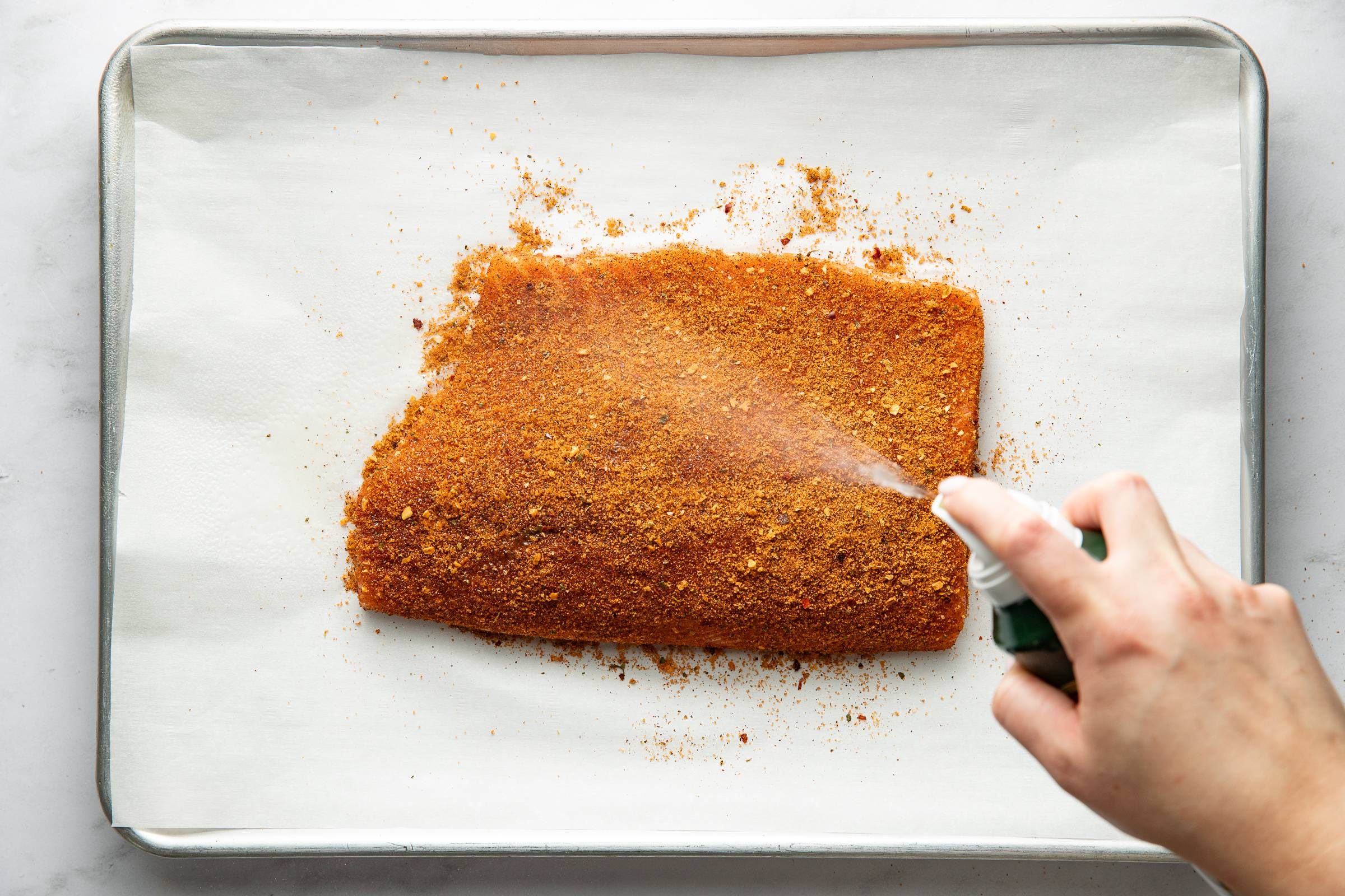 Spraying salmon with oil over a spice rub.