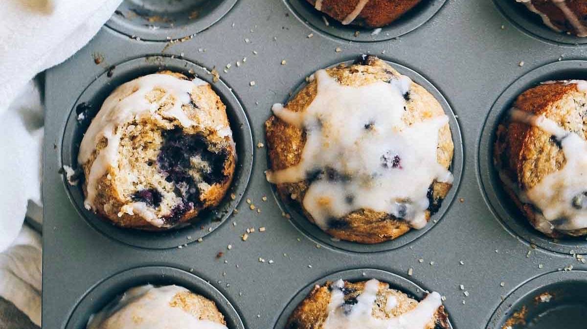 Whole Wheat Blueberry Muffins in a muffin tin with glaze.