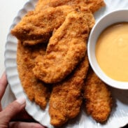 Chicken tenders on a plate with sauce on the side.