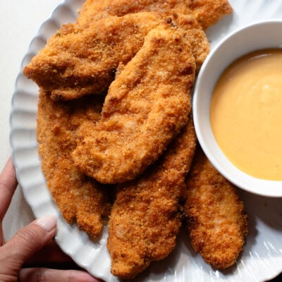 Chicken tenders on a plate with sauce on the side.