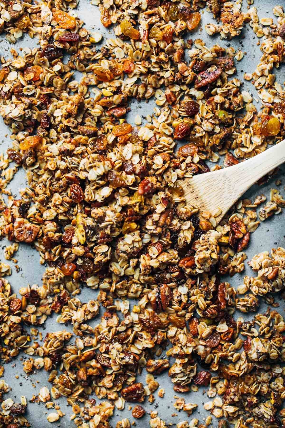 Coconut Oil Granola on a sheet pan with a wooden spoon.
